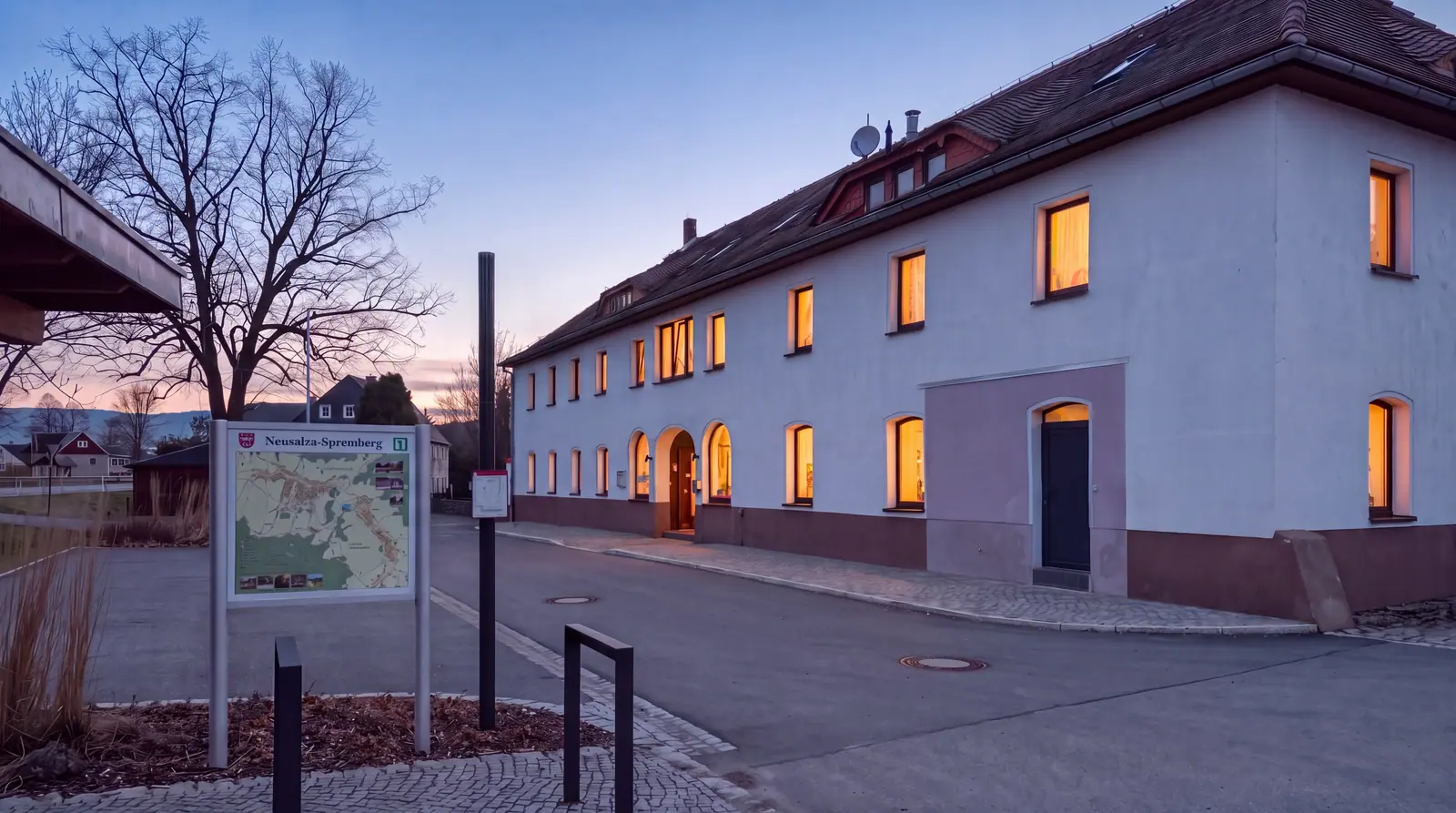Das Hotel Neusalza an der Talstraße in der Abenddämmerung: weißes Haus mit Satteldach und warm erleuchteten Bogenfenstern